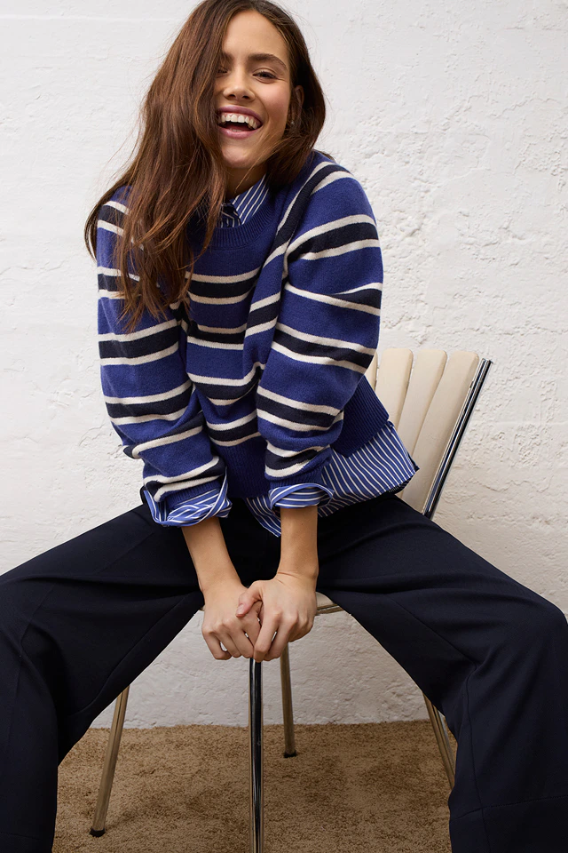 Women’s fashion from Oui, featuring a striped blouse worn under a striped knitted jumper, paired with dark blue trousers.