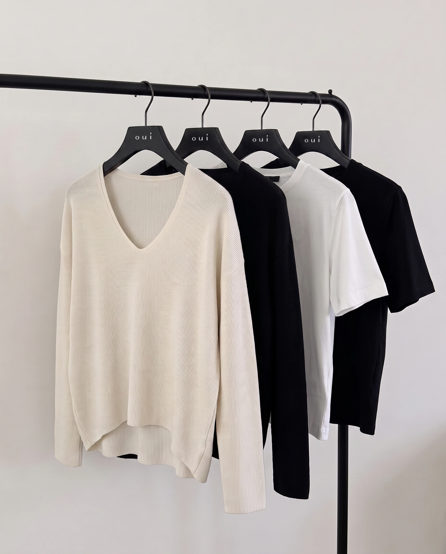 Oui Essentials: Women’s fashion featuring a cream-coloured V-neck jumper and black and white T-shirts on hangers