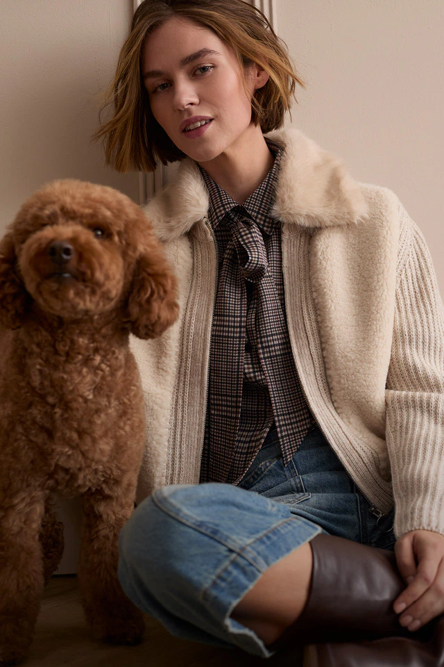 Model mit beiger Jacke mit Teddykragen, Karobluse und Jeans.