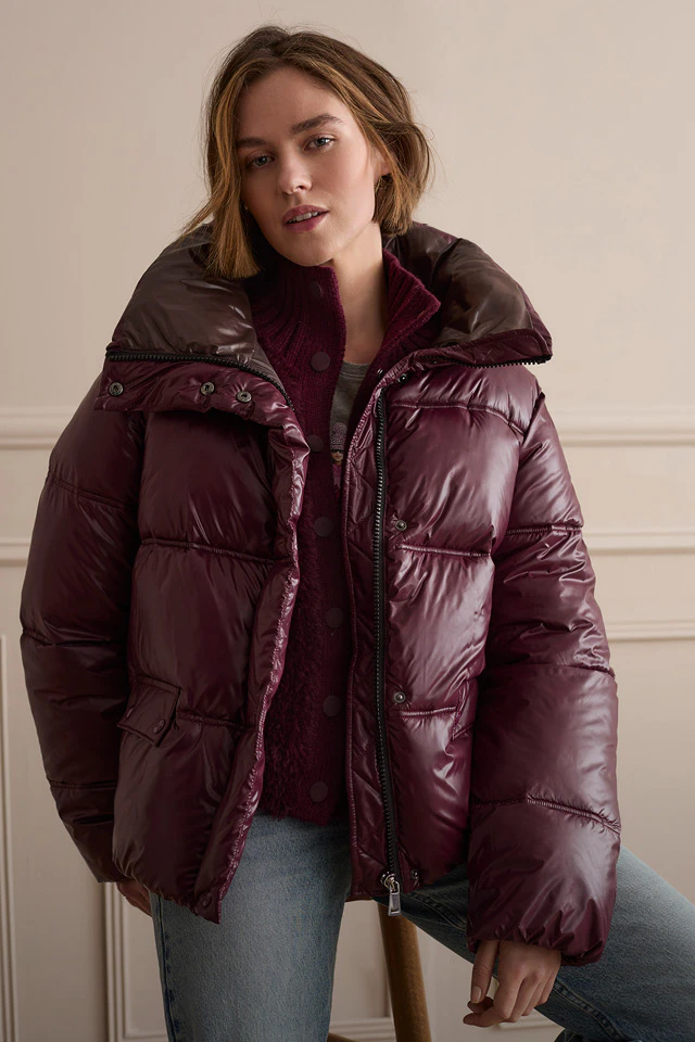Model trägt eine Pufferjacke mit einer Strickjacke darunter in Bordeauxrot.