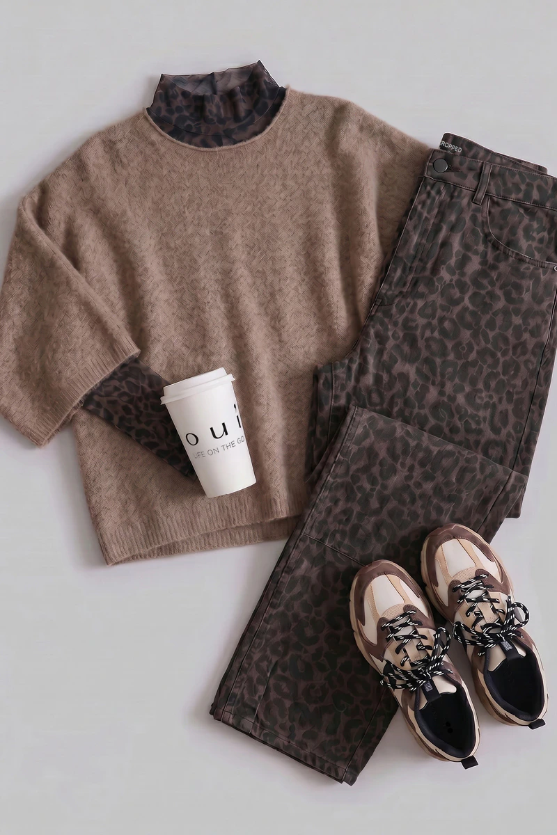 A women’s outfit from Oui featuring a knitted jumper, a blouse and patterned trousers.