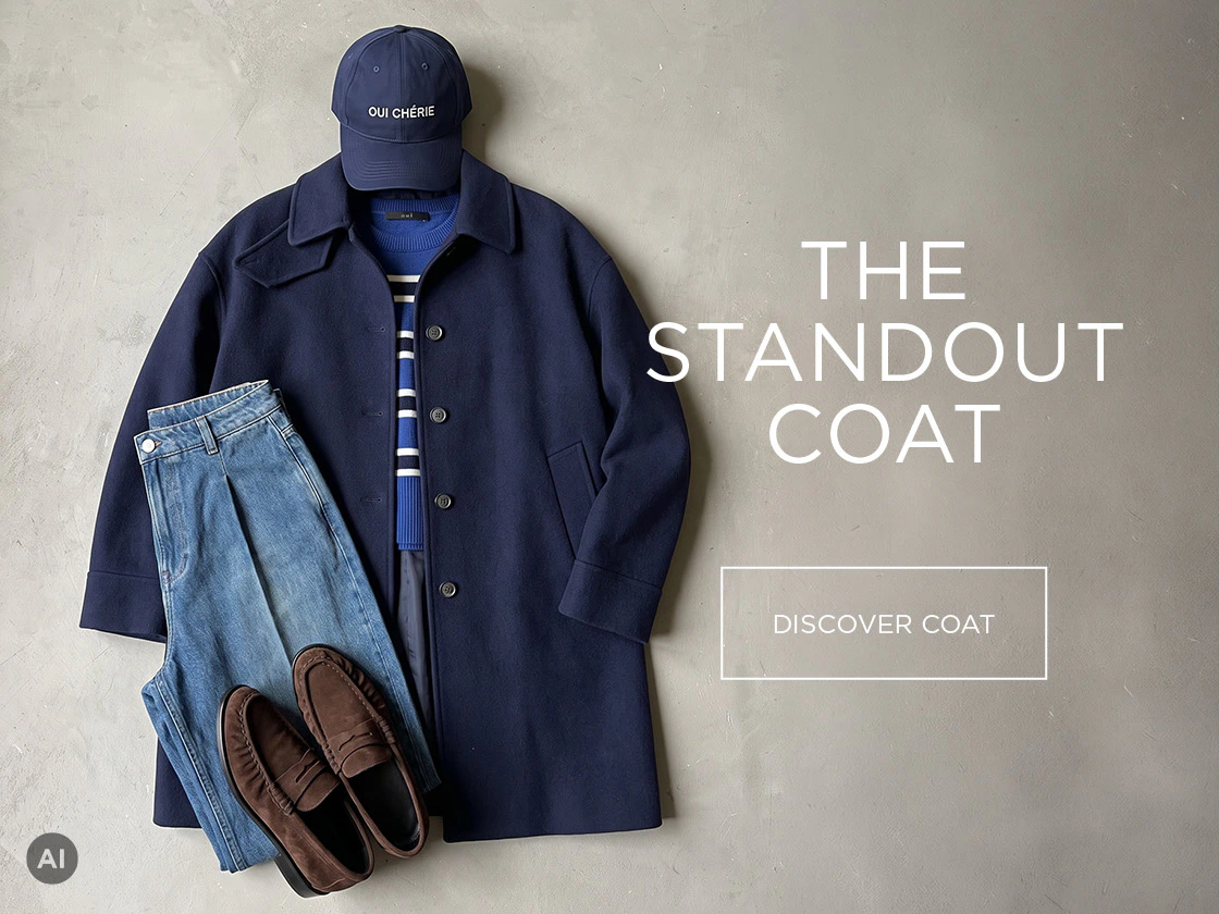 A classic navy-coloured coat by Oui, paired with a blue striped jumper, jeans, a cap and brown loafers, set against a neutral background.