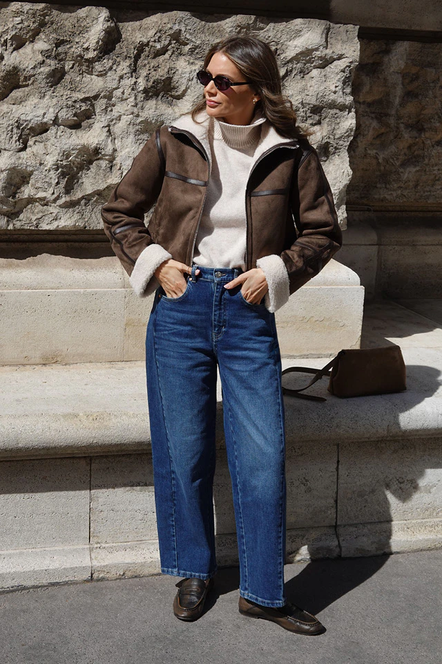 Influencer Raffaela Wachter in an Oui look, wearing a cream-coloured jumper, a brown leather jacket and dark blue jeans.