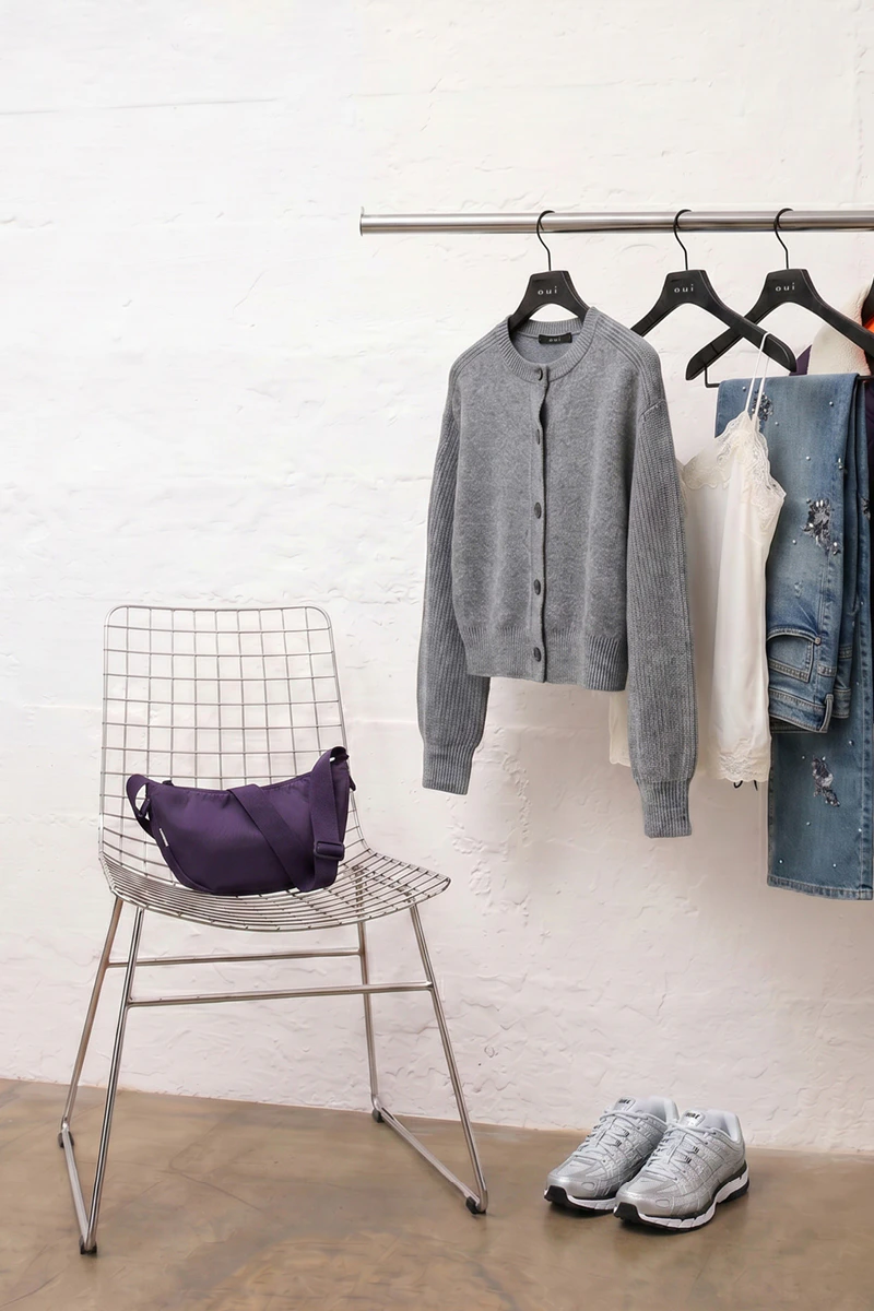 Clothes on a rail: a grey cardigan, behind it a white top with lace, and a pair of jeans.