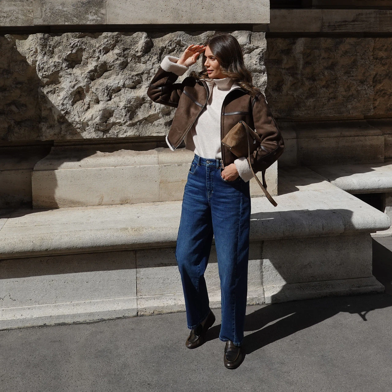 Influencer Raffaela Wachter in an Oui look, wearing a cream-coloured jumper, a brown leather jacket and dark blue jeans.