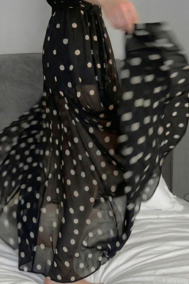 A close-up of the flowing skirt of a black dress with white dots.
