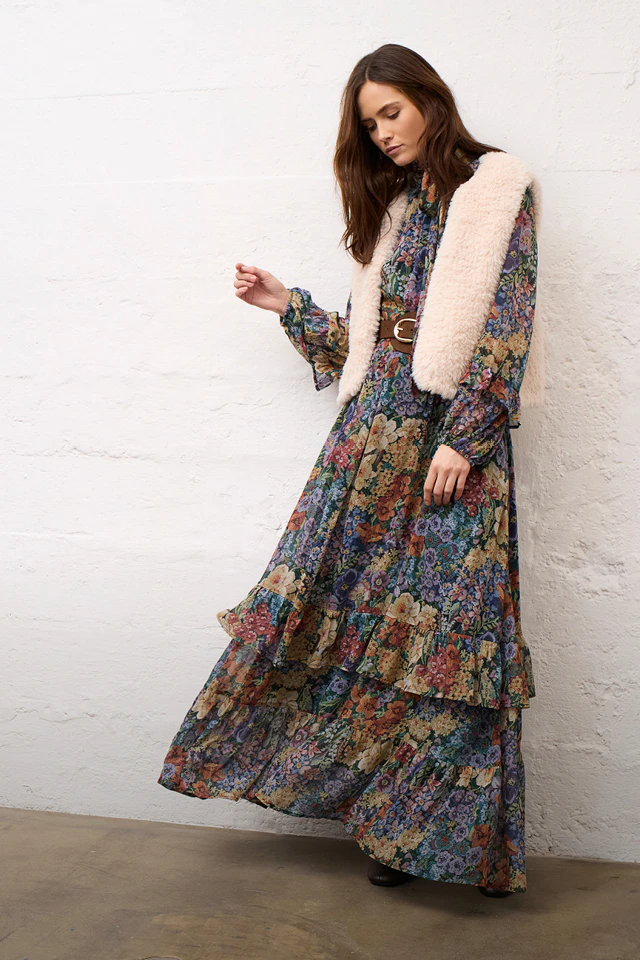 A woman wearing a floral midi dress and a beige waistcoat.