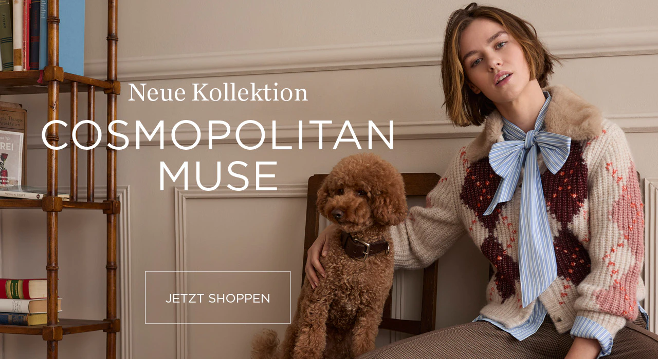 Neue Kollektion: Cosmopolitan Muse. Model trägt einen gemusterten Strickpullover über einer gestreiften Bluse mit Schleife und einen karierten Rock. Neben ihr sitzt ein brauner Hund.