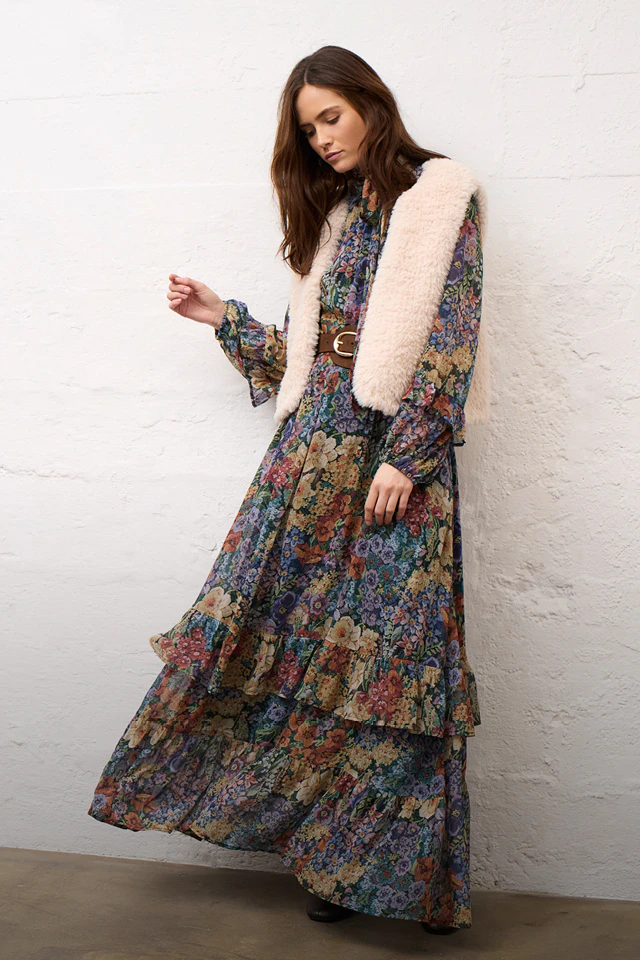 Eine Frau, die ein Midi-Kleid mit Blumenmuster und eine beige Weste trägt.