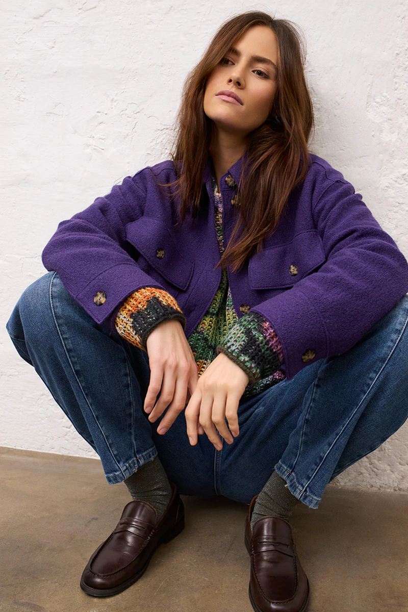Frau mit lila Jacke und einem gestrickten Pullover und Jeans.