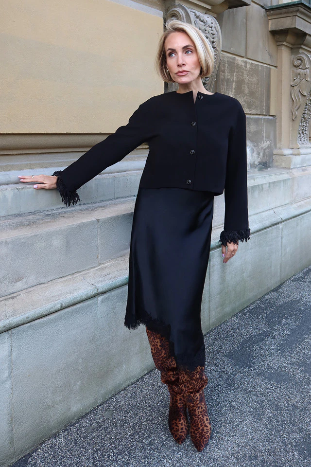Influencer Sophia Thorer is wearing an all-black outfit comprising a jacket and a satin skirt with a lace hem.