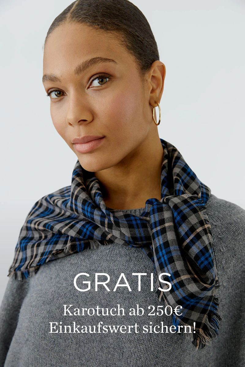 Model in grauem Strickpullover mit blau-grau kariertem Tuch aus der OUI Heritage Reset Kollektion - ergänzt durch den Hinweis „Gratis Karotuch ab 250 € Einkaufswert sichern“.