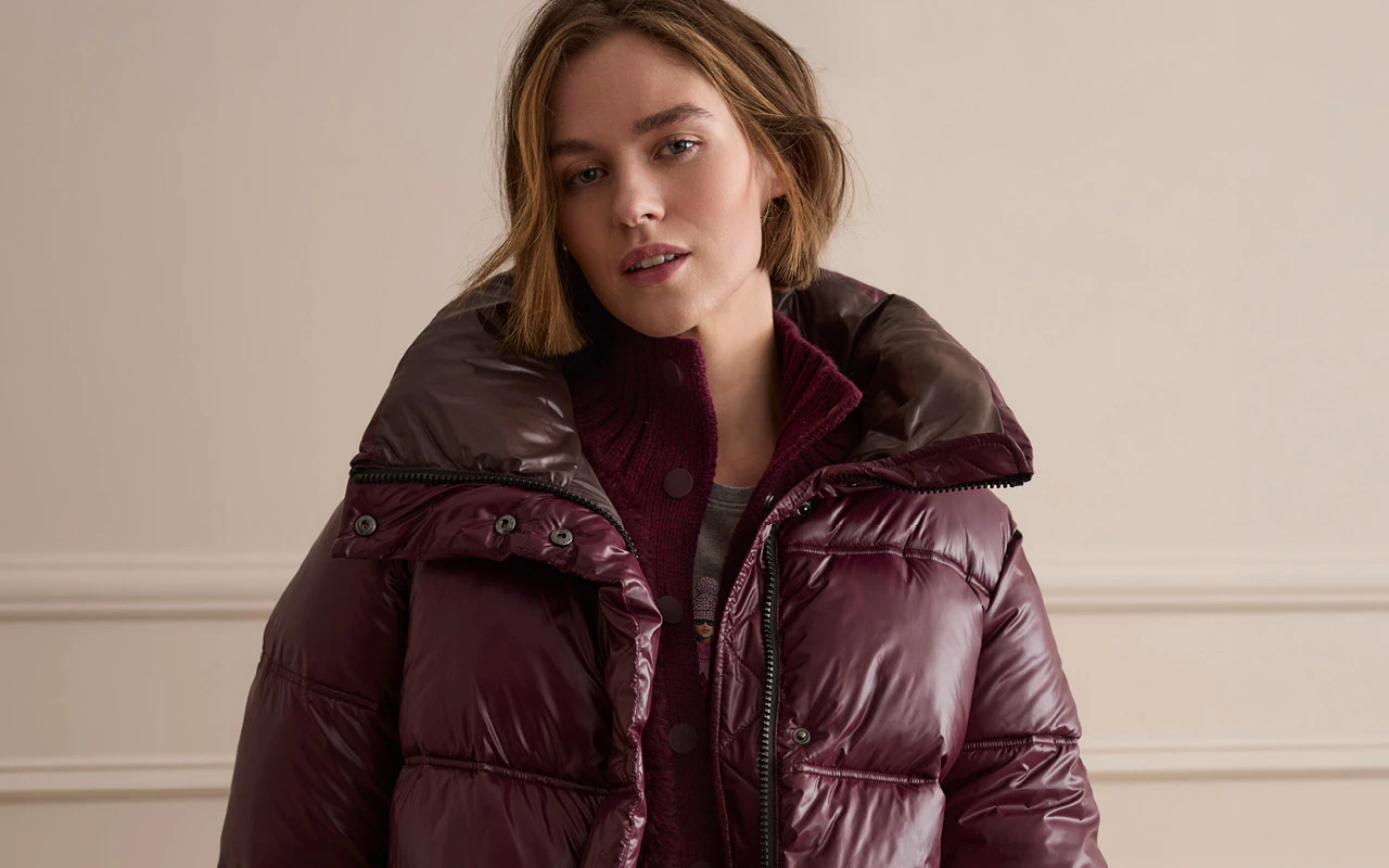 Model trägt eine Pufferjacke mit einer Strickjacke darunter in Bordeauxrot.