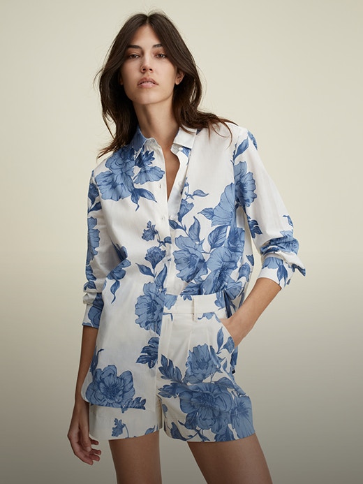 Frau mit All over Blumen Outfit. Bluse in weiss mit blauen Blumendruck, dazu eine passende Short ebenfalls in weiss mit blauem Blumendruck.