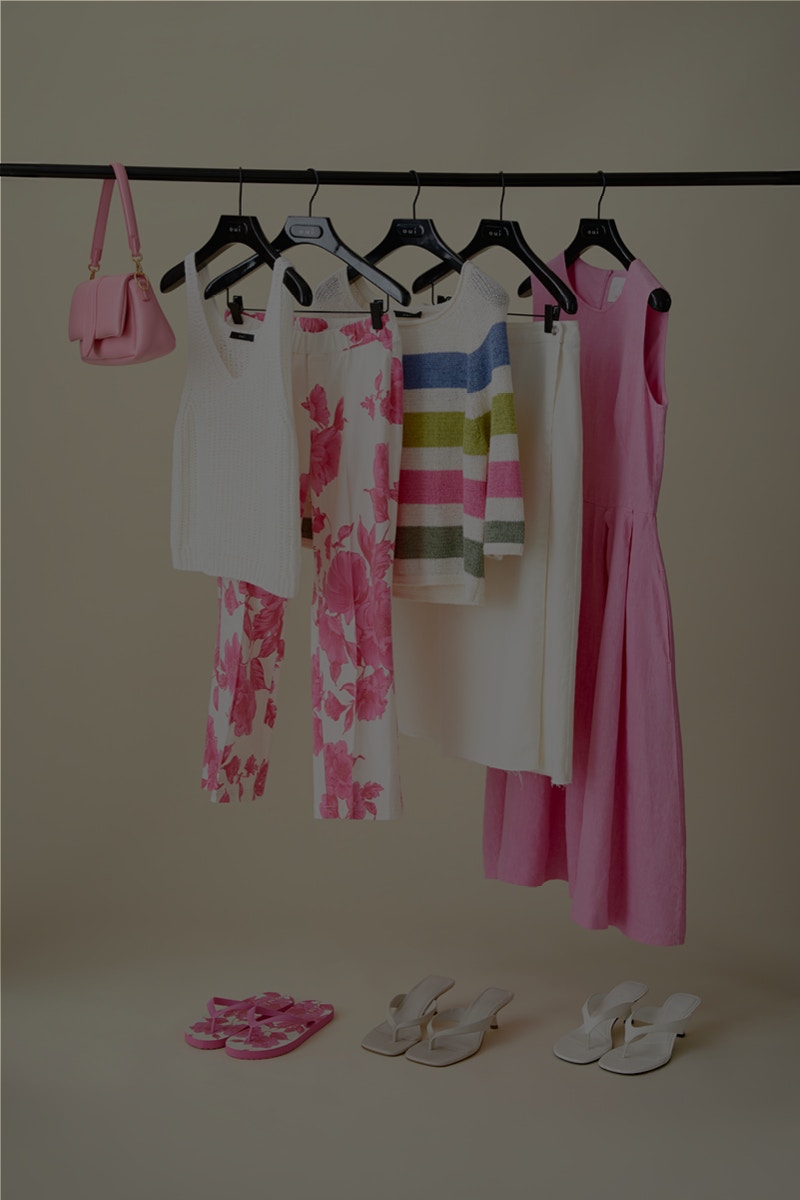 Kleiderstange mit weißem Top, Hose in pinkem Blumendruck, blockstreifen Pullover, weißer Rock und einem pinken Kleid.