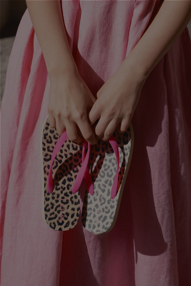 Women's hands holding 2 flip*flops with leather print in the insole and pink straps.