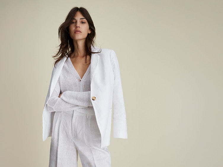 Woman with white blazer, white cardigan and white trousers.