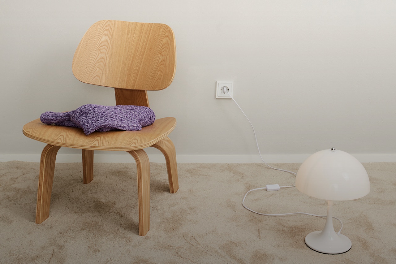 A wooden chair on the left with a purple jumper folded on top. A white lamp on the right and everything on a beige-coloured carpet.