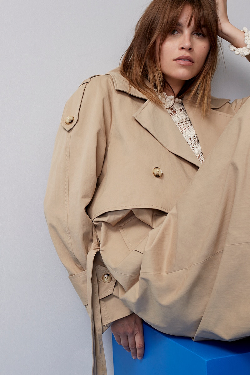 Woman with a beige trench coat and a white crocheted top underneath.