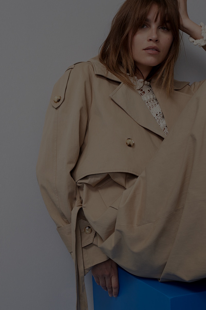 Woman with a beige trench coat and a white crocheted top underneath.