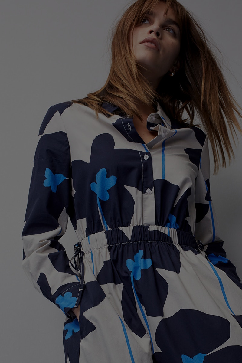 Woman with dress in white base colour and on it large flowers in dark blue with light blue.