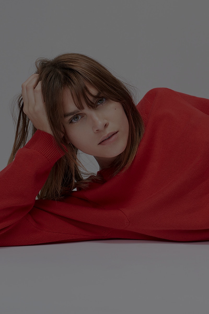 Reclining woman wearing a red pullover and resting her head on one hand.