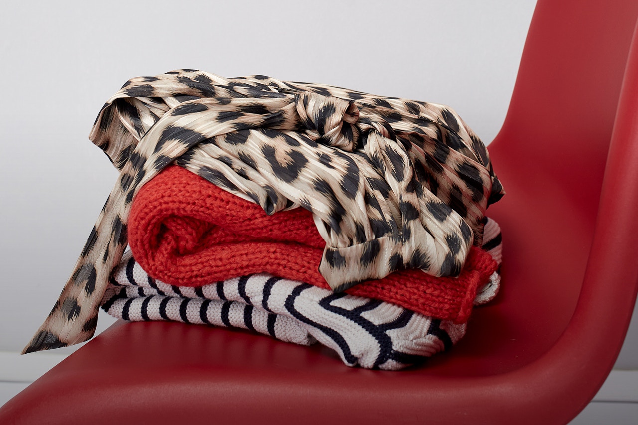 Red chair with a pile of pullovers in leopard print, red and white and black stripes.
