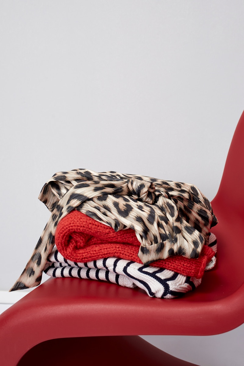 Roter Stuhl mit einem Stapel Pullover in Leopardenmuster, rot und weiss schwarz gestreift.
