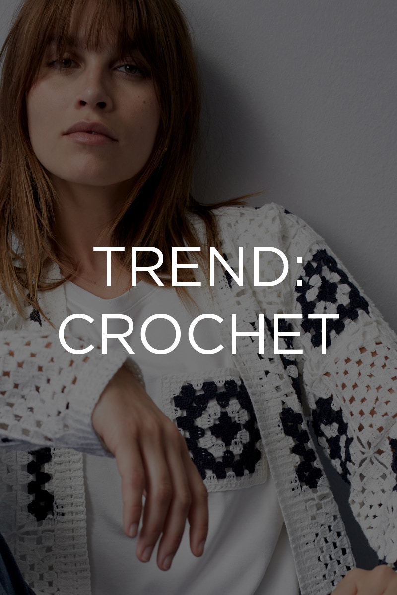 Woman wearing a white T-shirt with black embroidery on a small breast pocket and a white crocheted cardigan with black crocheted flowers.