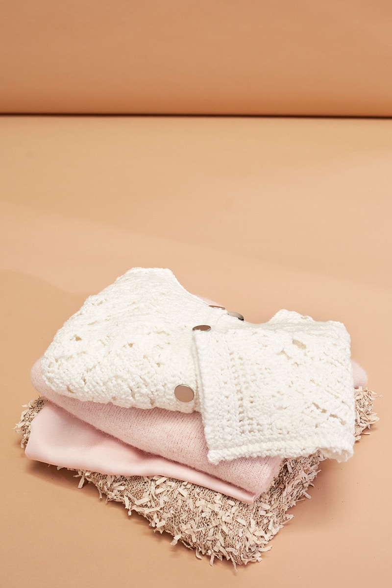 Ein Stapel Pullover in unterschiedlichen Farben und Strukturen. Gehalten in weiss, rosa und beige.