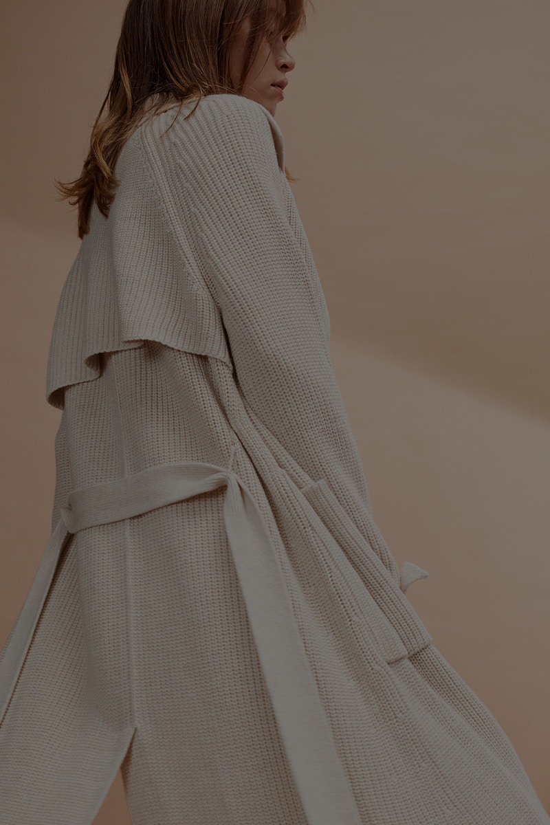 Frau seitlich mit einem langen Mantel in weiß.