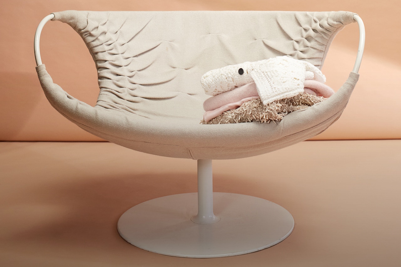 A white modern chair with a pile of knitted pullovrs and tops in muted colours of white, rosé and brown.