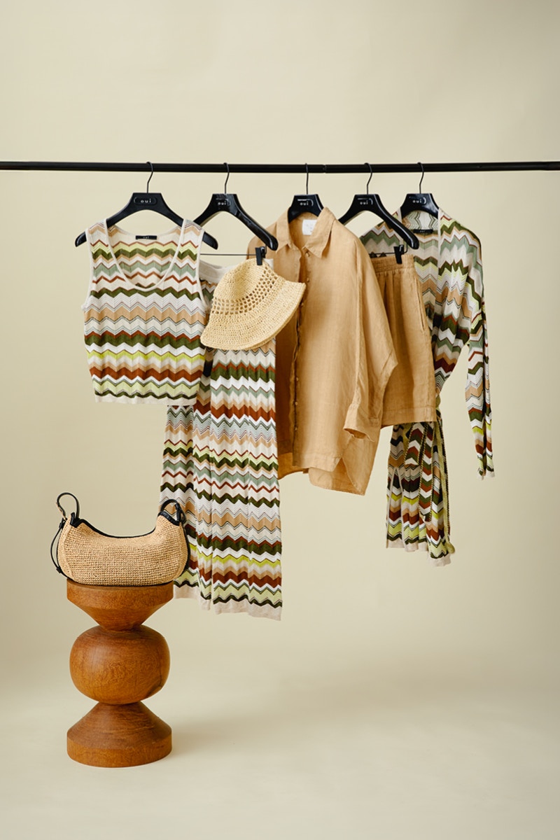 Clothes rail with top, skirt and cardigan in zigzag pattern in various colors such as brown, white, beige and green. In between hangs a blouse and shorts in brown.