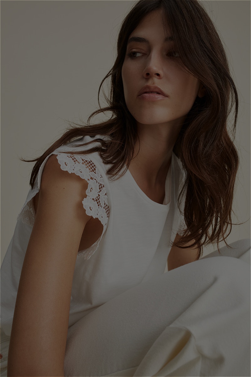 Woman wearing a white top with frilly sleeves and white trousers.