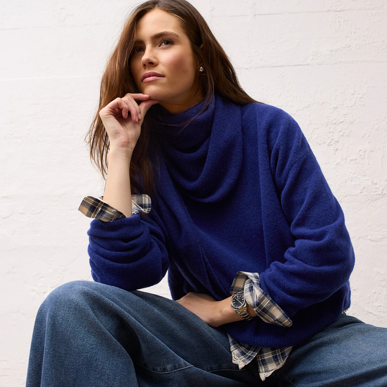 Model trägt einen blauen Pullover mit weitem Kragen, darunter eine karierte Bluse und eine weite Jeans aus der Oui Heritage Reset Kollektion.