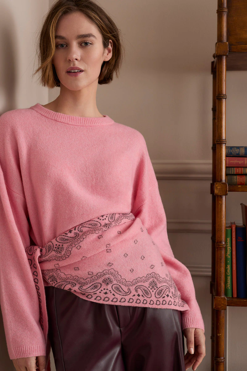 Model trägt einen rosafarbenen Strickpullover mit passendem Tuch und eine dunkelrote Hose.