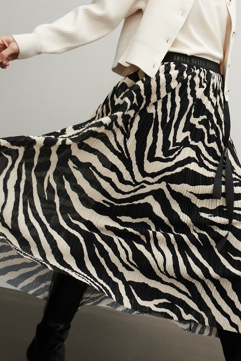 A detail of a woman without a head. Shown is a curved maxi skirt in a black and white zebra pattern. She is wearing a white jacket and a white top.