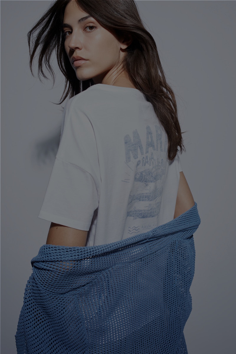 Woman wearing a white T-shirt with a print on the back and a blue cardigan.