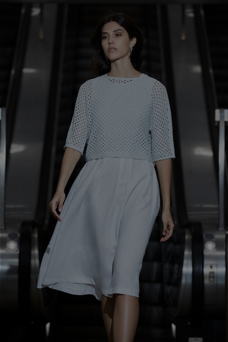 Woman wearing a light blue crocheted jumper with 3/4 sleeves and a midi dress also in light blue underneath.