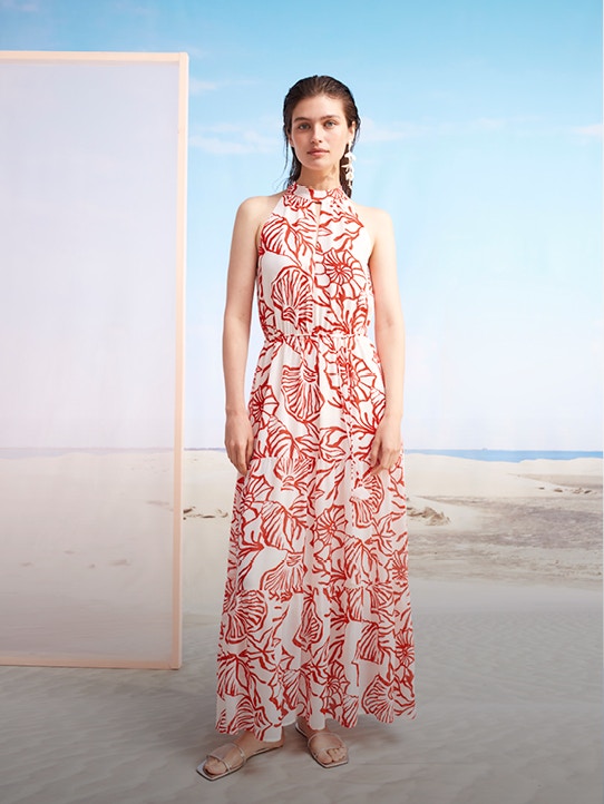 Woman on the beach wearing a maxi dress in white with a red shell print.