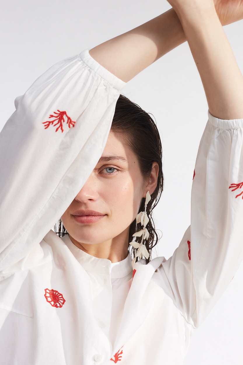 Woman with a white blouse with red embroidered elements shells and corals.