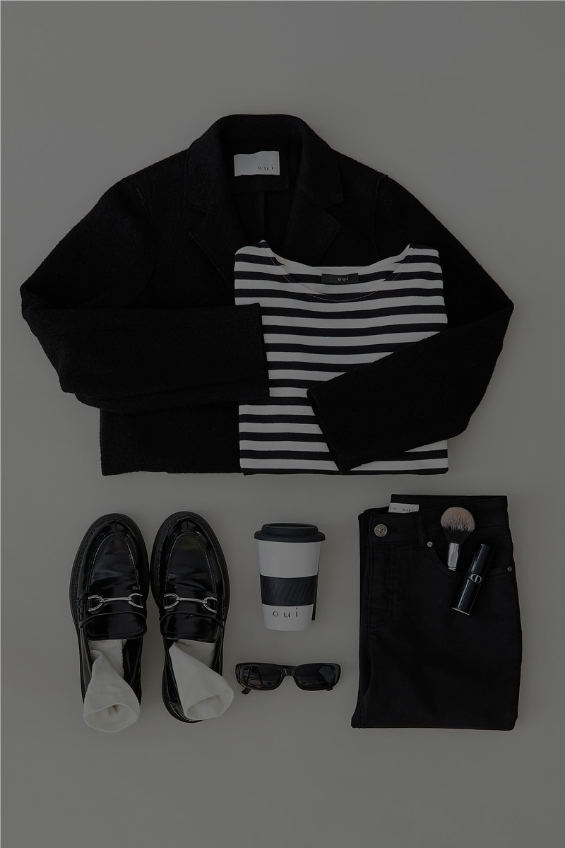 Ein Bild von oben fotografiert mit einer schwarzen Jacke die rechts ein gestreiftes Langarmschirt hat, darunter ein paar Loafer links, ein Kaffebecher mit einer Sonnerbrille in der Mitte und rechts eine schwarze Hose.