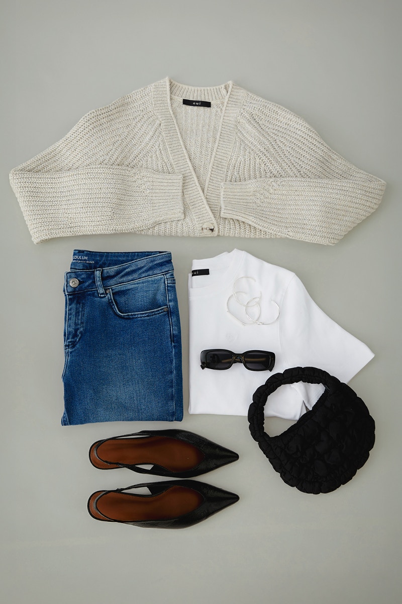 A picture from above on folded clothes. A beige cardigan on top, a folded pair of blue jeans on the left and a folded white T-shirt on the right, completed with sunglasses, a bag and sandals.