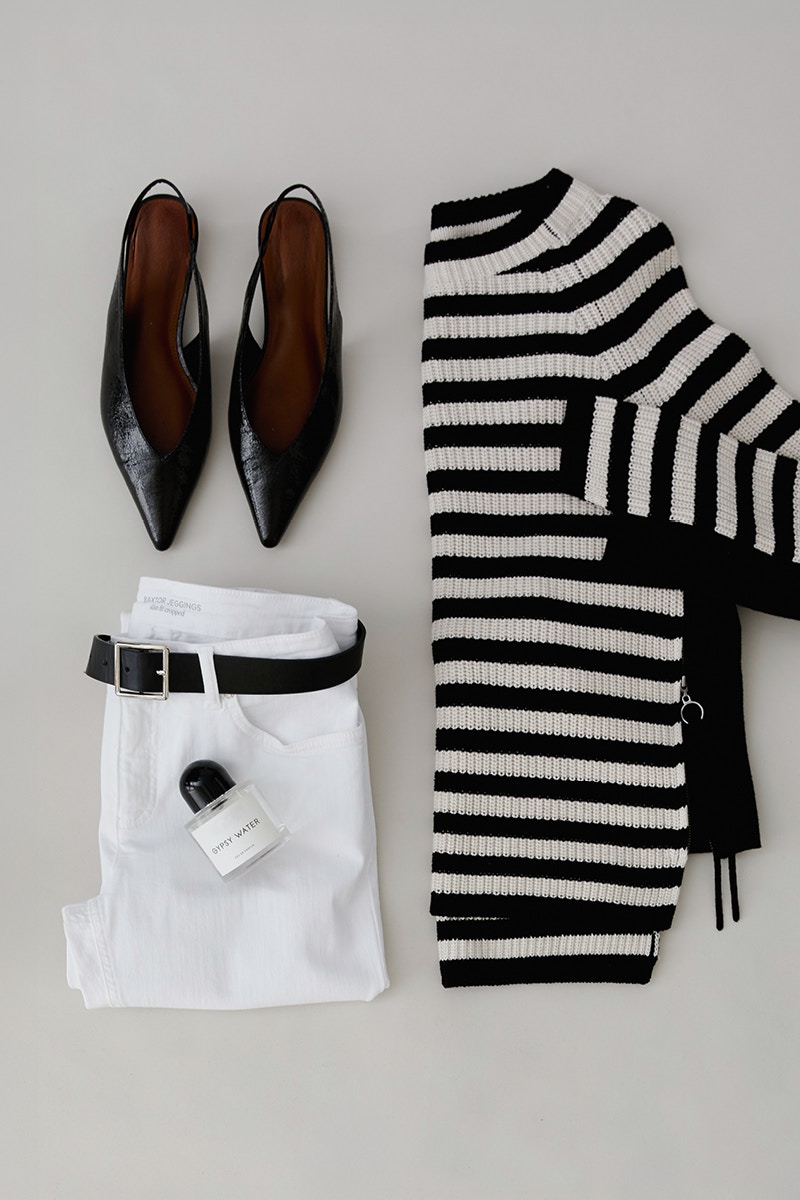 A picture taken from above shows a half-folded jumper in black and white on the right, a pair of sandals on the top left and white trousers underneath.