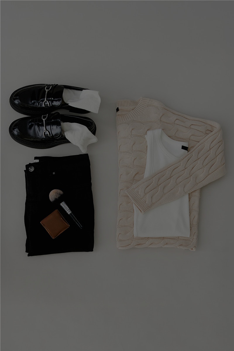 A picture taken from above with the clothes laid out. Top left a pair of loafers in black, underneath black trousers with make-up accessories and next to it on the right a beige jumper with a white top on top. The picture refers to a magazine article about the Oui Essentials.
