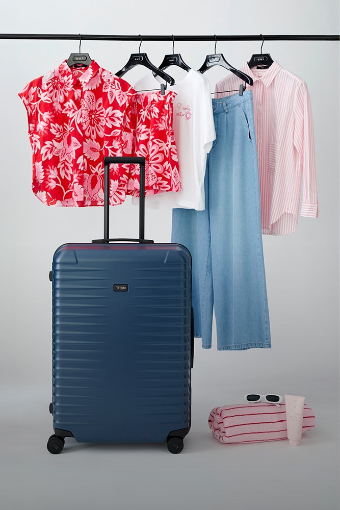 Ein Bild mit einem blauen Titan Koffer vor einer Kleiderstange mit diversen Bekleidungsstücken. Es verweist auf ein Gewinnspiel