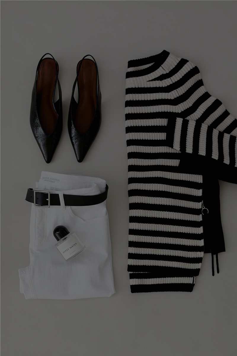 Ein Bild von oben fotographiert zeigt rechts einen halb gefalteten Pullover in schwarz/weiß, links oben ein paar Sandalen und darunter eine weiße Hose.