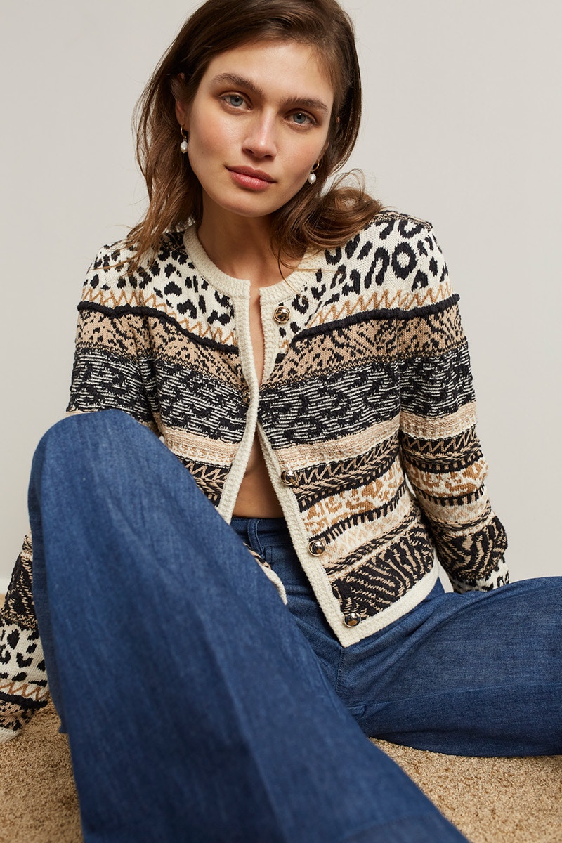Sitting woman wearing a cardigan in block stripes with different patterns with jeans trousers.