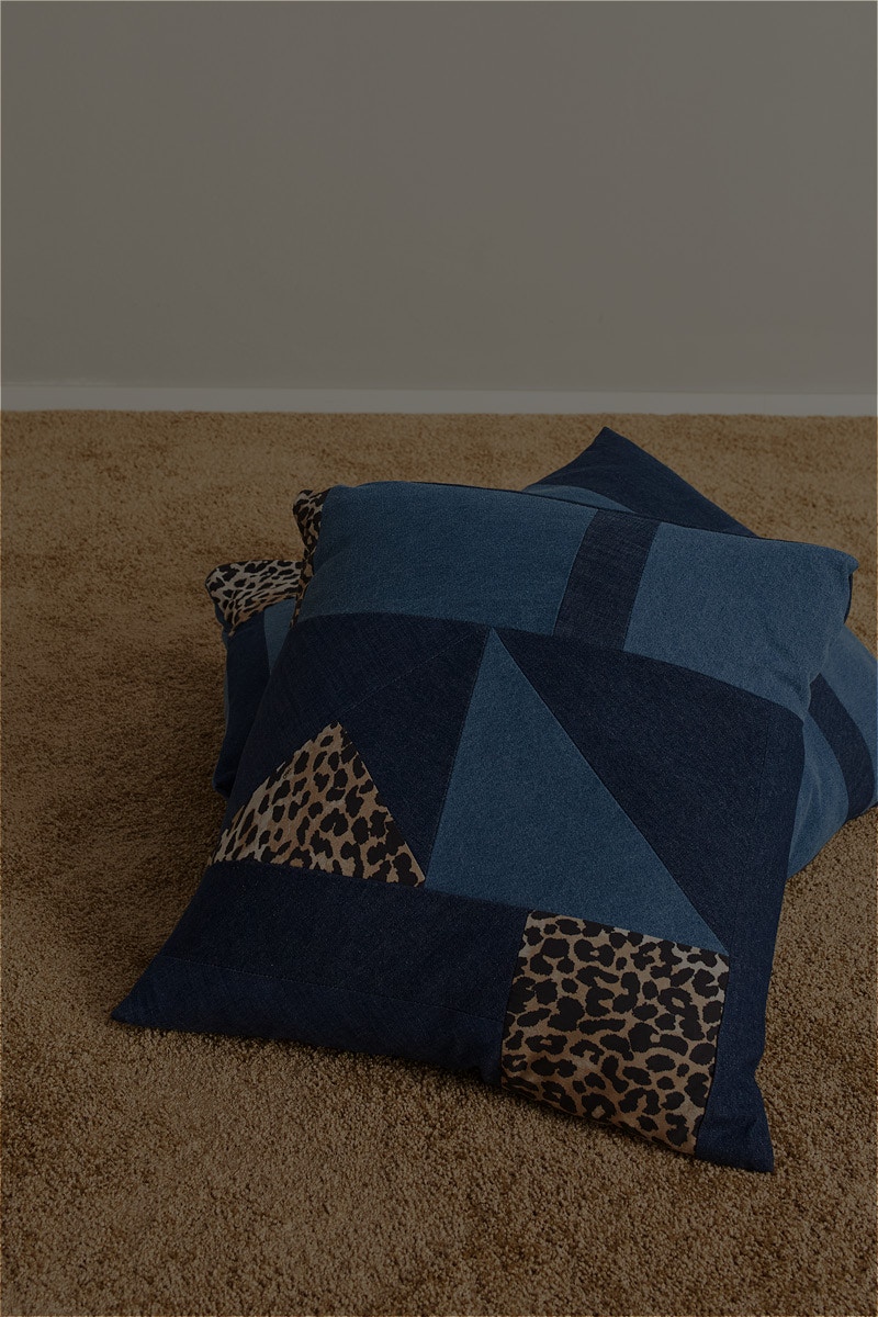 Two cushions in denim and leopard patches lie on a plush brown rug.