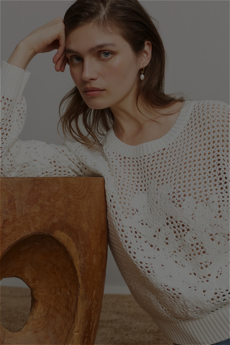 Woman wearing a white crochet-look jumper with a pattern.